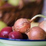 A rustic still life featuring onions and apples on a plate.